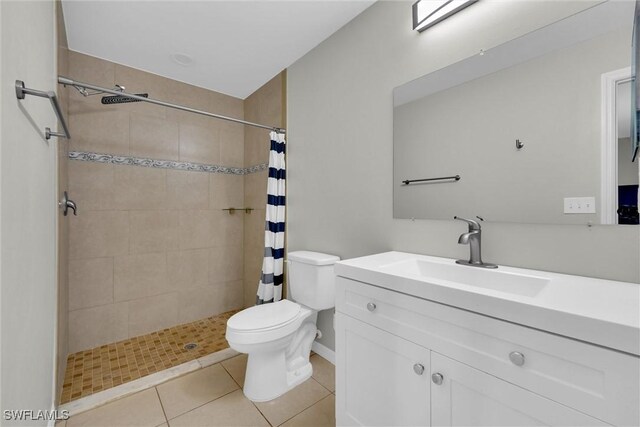 bathroom with toilet, tiled shower, tile patterned flooring, and vanity