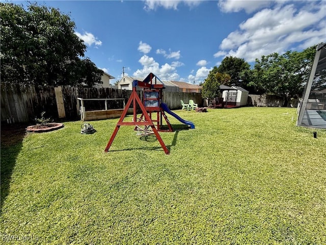 view of playground featuring a lawn, an outbuilding, a storage unit, and a fenced backyard