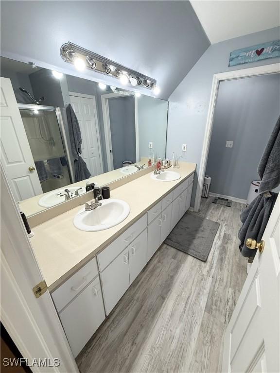 full bathroom featuring double vanity, a sink, a stall shower, and vaulted ceiling