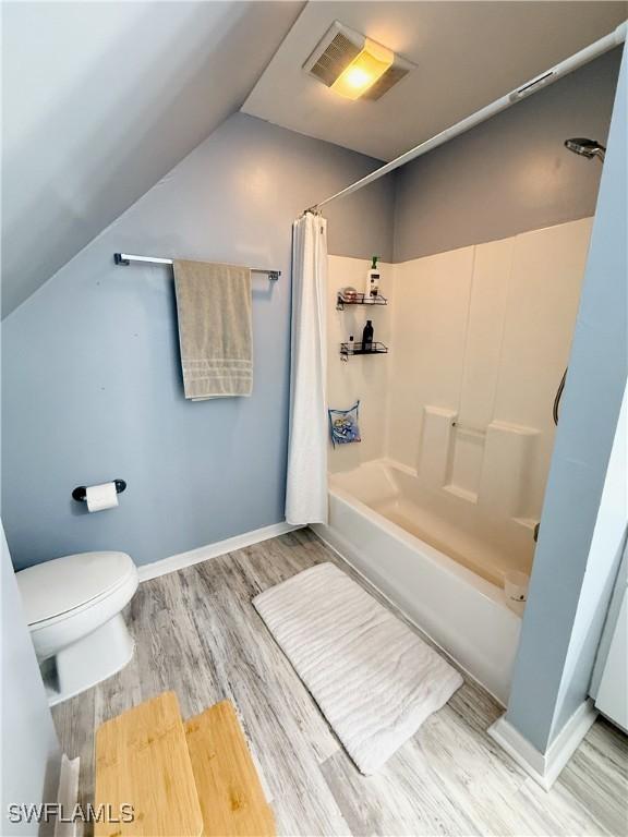 bathroom with toilet, shower / bath combo, wood finished floors, lofted ceiling, and visible vents