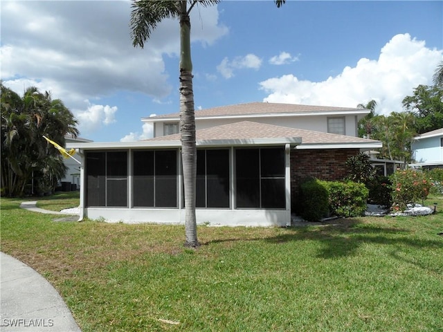 back of property featuring a sunroom, roof with shingles, brick siding, and a yard