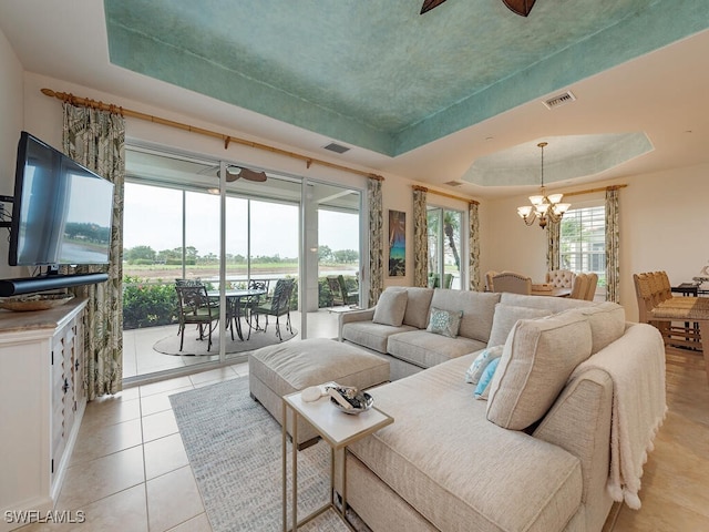 living area with visible vents, light tile patterned floors, an inviting chandelier, and a tray ceiling