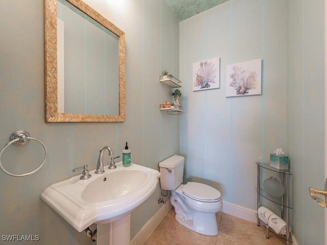 half bathroom with a sink, toilet, tile patterned flooring, and baseboards