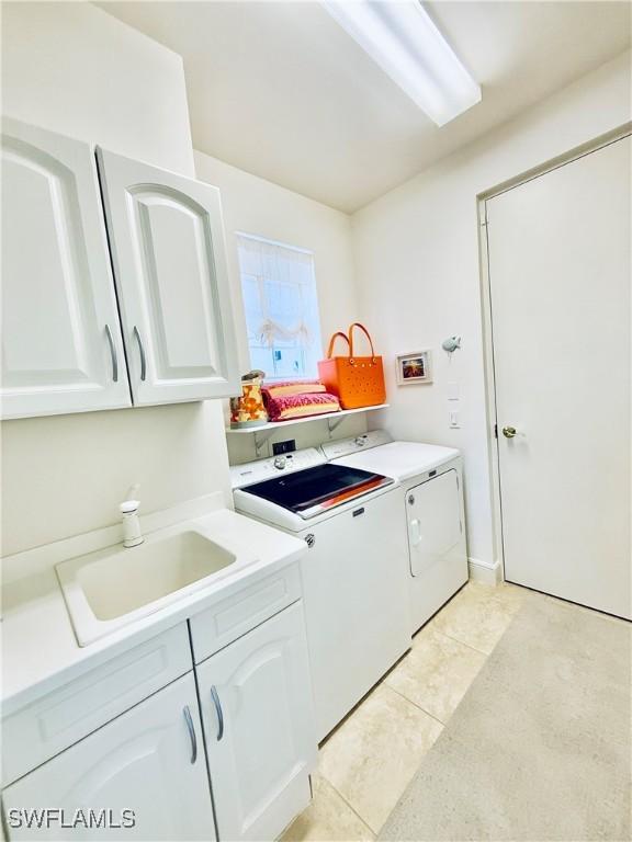 laundry area with light tile patterned floors, separate washer and dryer, cabinet space, and a sink