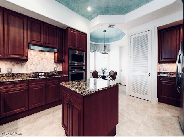 584 Avellino Isles Cir Unit 19102, Naples, FL 34119 - kitchen featuring appliances with stainless steel finishes, under cabinet range hood, reddish brown cabinets, dark stone counters, and decorative backsplash