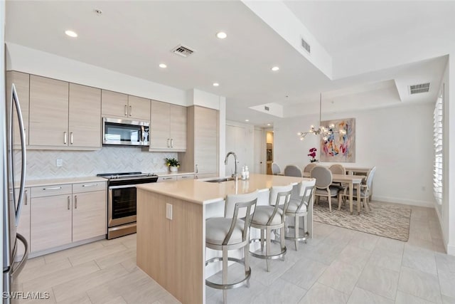 1111 Central Ave Unit 507, Naples, FL 34102 - kitchen with stainless steel appliances, a sink, a breakfast bar area, an island with sink, and backsplash