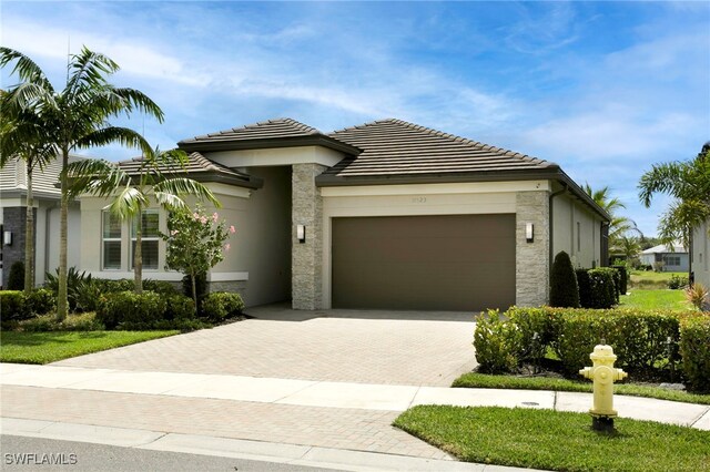 view of front facade featuring a tile roof, a garage, stone siding, decorative driveway, and stucco siding