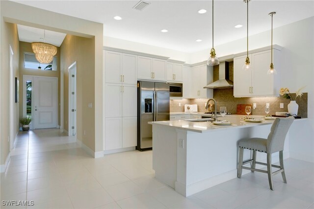 kitchen with stainless steel appliances, visible vents, a peninsula, wall chimney range hood, and backsplash