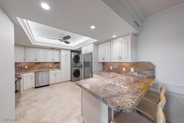 174 S Collier Blvd Unit 504, Marco Island, FL 34145 - kitchen featuring stacked washer / dryer, appliances with stainless steel finishes, a tray ceiling, a peninsula, and crown molding