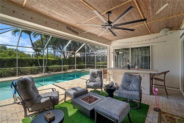 outdoor pool featuring ceiling fan, glass enclosure, an outdoor fire pit, a patio, and outdoor dry bar