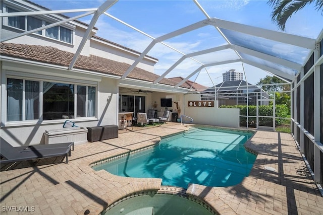 view of swimming pool featuring ceiling fan, a pool with connected hot tub, a patio, and glass enclosure