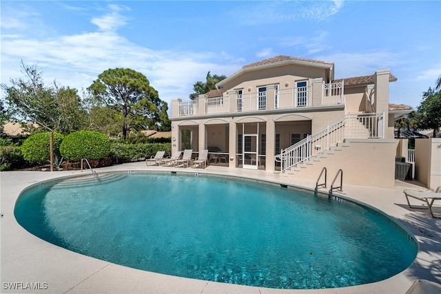 back of house featuring stucco siding, stairway, a patio area, a balcony, and an outdoor pool