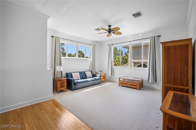 living room featuring ceiling fan, baseboards, ornamental molding, and visible vents