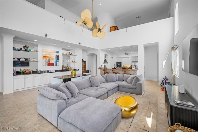 living room with bar, a ceiling fan, arched walkways, and a towering ceiling