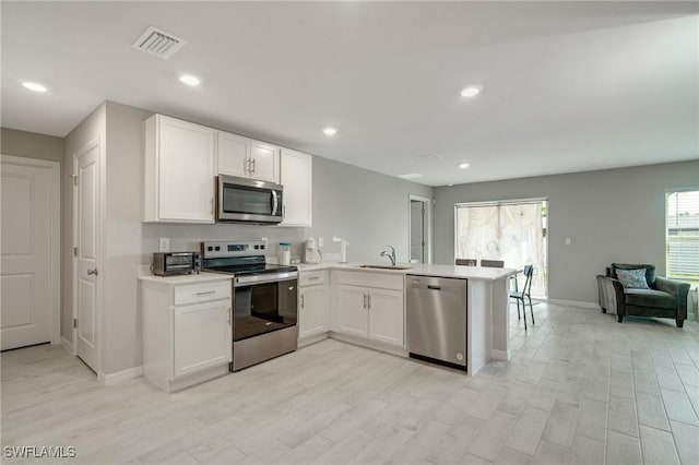 kitchen with white cabinetry, light countertops, stainless steel appliances, visible vents, and a peninsula