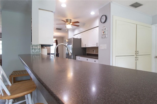 77 Cardinal Dr, North Fort Myers, FL 33917 - kitchen featuring a ceiling fan, dark countertops, a kitchen bar, freestanding refrigerator, and white cabinets