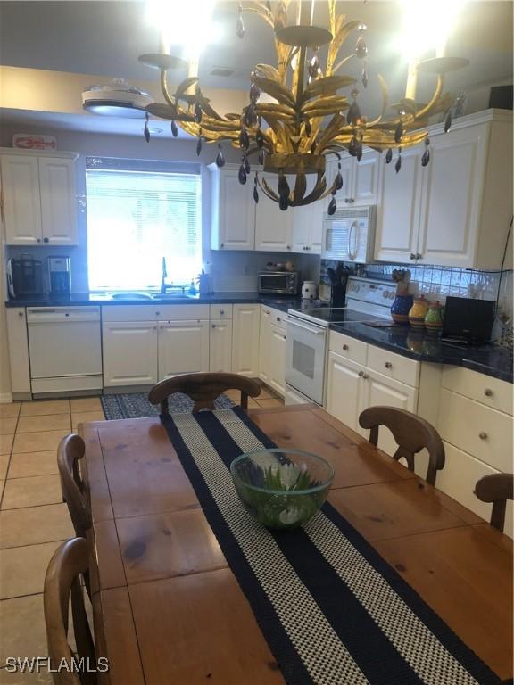 kitchen with a chandelier, dark countertops, white cabinetry, and white appliances