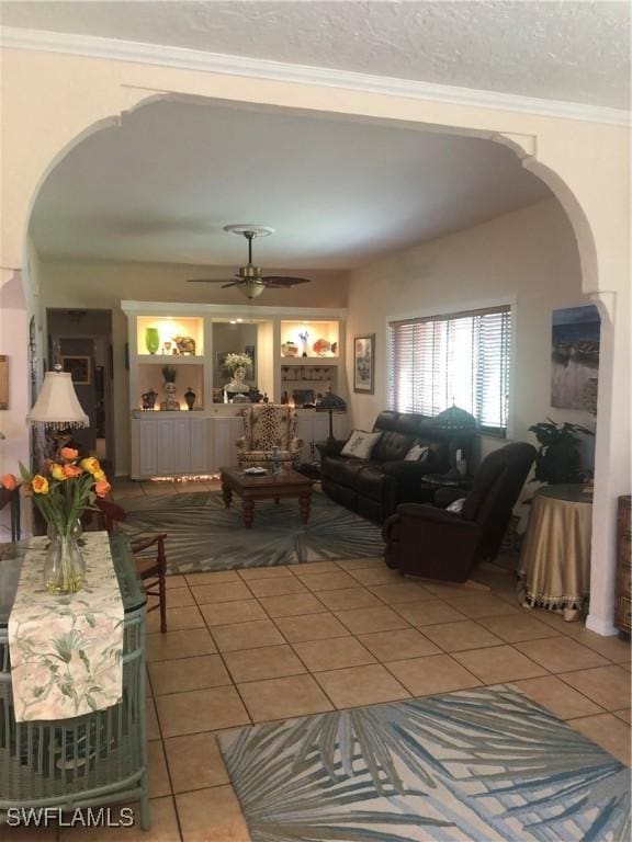 tiled living room with arched walkways, ceiling fan, and crown molding