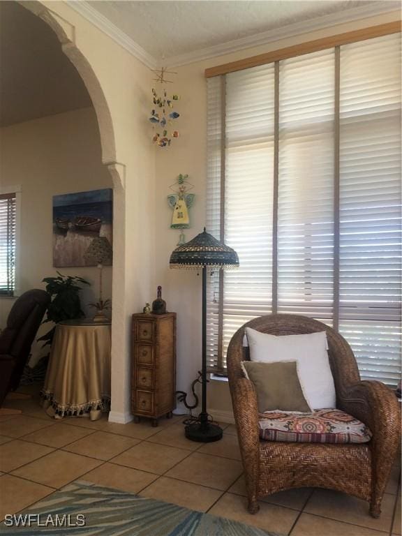 sitting room with arched walkways, crown molding, tile patterned floors, and baseboards