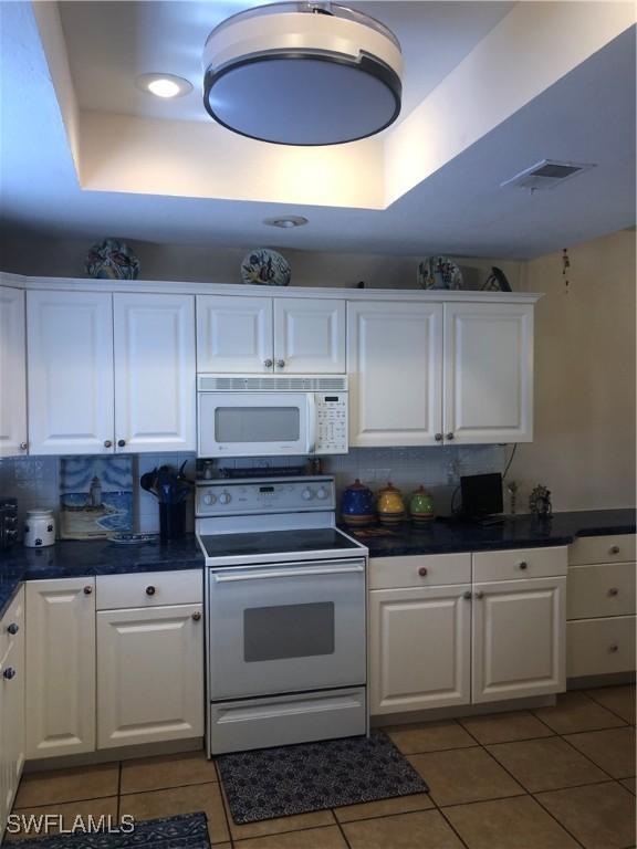 kitchen featuring white cabinets, dark countertops, white appliances, and light tile patterned floors
