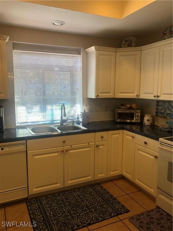kitchen with white cabinets, tile patterned floors, a sink, and white appliances