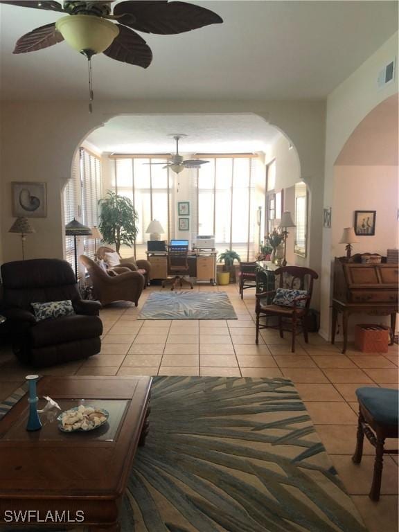 living room featuring tile patterned floors, a ceiling fan, visible vents, and arched walkways