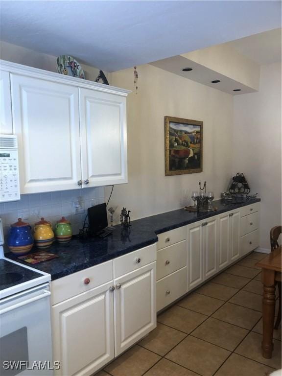 kitchen featuring dark countertops, white cabinetry, decorative backsplash, white appliances, and light tile patterned floors