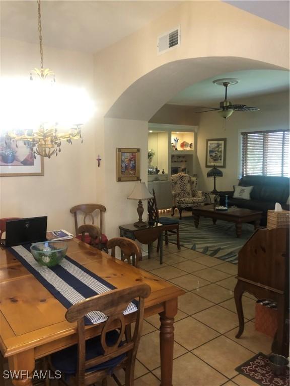 dining area featuring ceiling fan with notable chandelier, visible vents, arched walkways, and light tile patterned floors