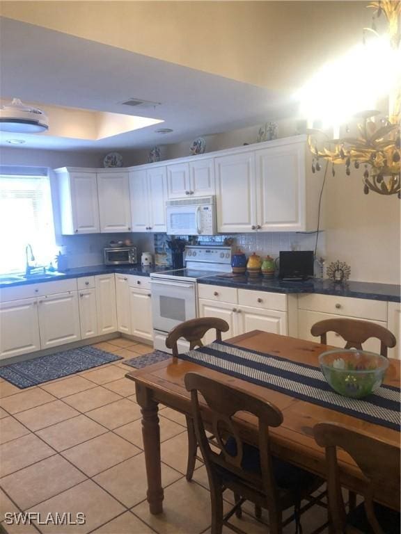 kitchen with dark countertops, a sink, white appliances, tasteful backsplash, and white cabinetry