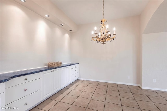unfurnished dining area with recessed lighting, light tile patterned floors, arched walkways, baseboards, and a notable chandelier
