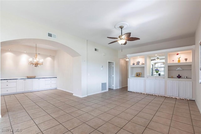 spare room with light tile patterned floors, arched walkways, visible vents, and ceiling fan with notable chandelier