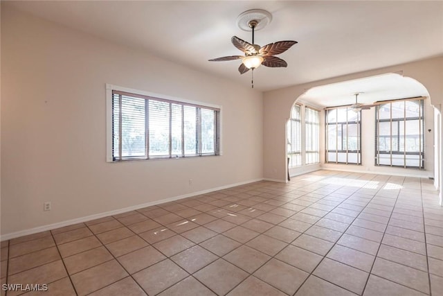 spare room featuring ceiling fan, arched walkways, a healthy amount of sunlight, and light tile patterned floors