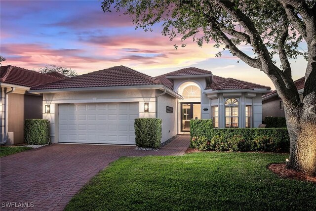 1002 Fountain Run, Naples, FL 34119 - mediterranean / spanish-style house featuring decorative driveway, an attached garage, a tiled roof, stucco siding, and a lawn