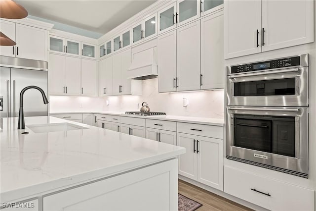 kitchen with premium range hood, backsplash, white cabinetry, light wood-style floors, and stainless steel appliances