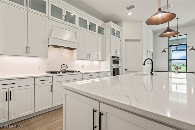 kitchen featuring premium range hood, gas cooktop, visible vents, double oven, and a sink
