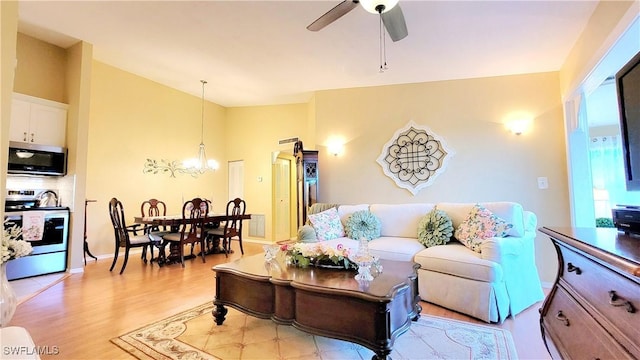 living room with light wood finished floors, ceiling fan with notable chandelier, and vaulted ceiling