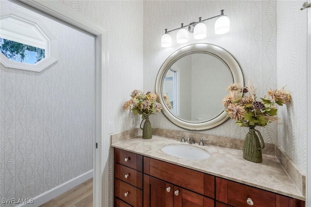 bathroom with vanity, wood finished floors, and wallpapered walls
