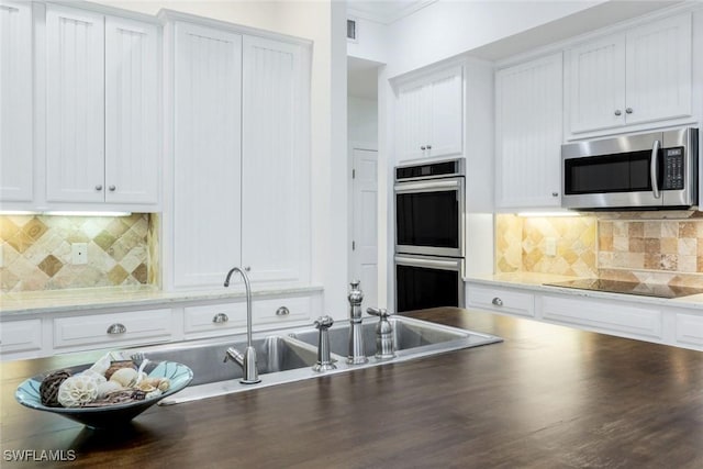 kitchen featuring white cabinets, decorative backsplash, ornamental molding, and appliances with stainless steel finishes