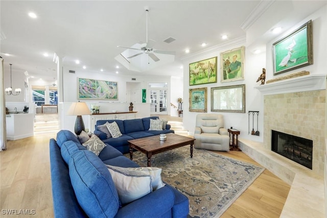 living area with recessed lighting, a fireplace with raised hearth, light wood-style floors, crown molding, and ceiling fan with notable chandelier