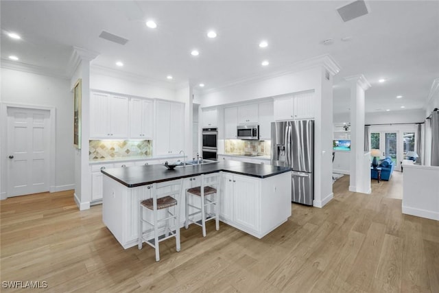 kitchen featuring dark countertops, appliances with stainless steel finishes, a large island with sink, and crown molding