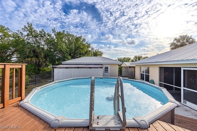 view of swimming pool featuring fence, a sunroom, an outbuilding, and a deck