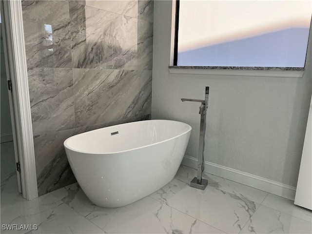 full bathroom featuring a freestanding bath, baseboards, and marble finish floor