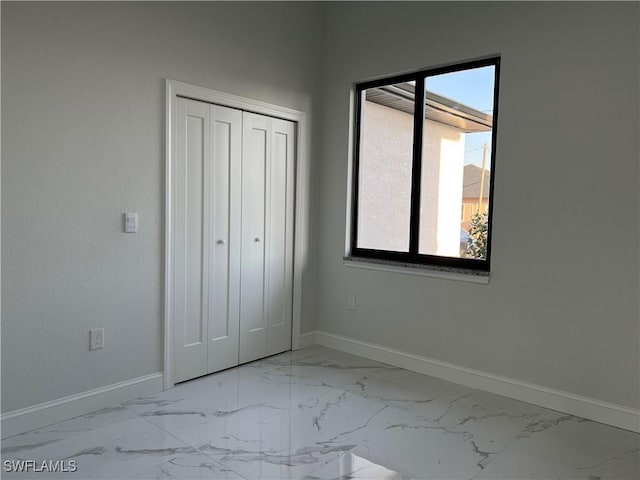 unfurnished bedroom featuring baseboards, marble finish floor, and a closet