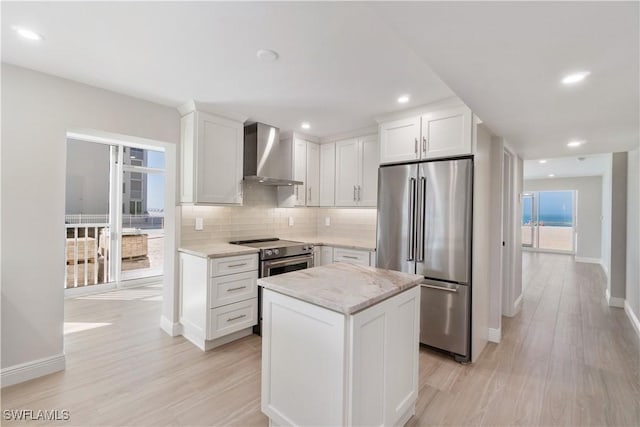 25900 Hickory Blvd Unit 101, Bonita Springs, FL 34134 - kitchen with stainless steel appliances, wall chimney range hood, light wood-type flooring, tasteful backsplash, and white cabinetry