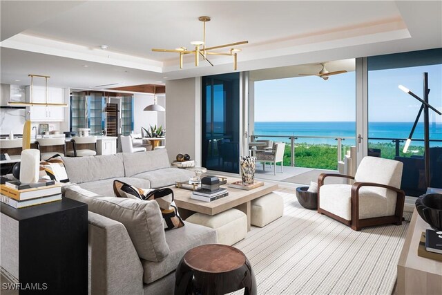 6897 Grenadier Blvd Unit 1602, Naples, FL 34108 - living room with a tray ceiling, ceiling fan with notable chandelier, a wall of windows, and a water view