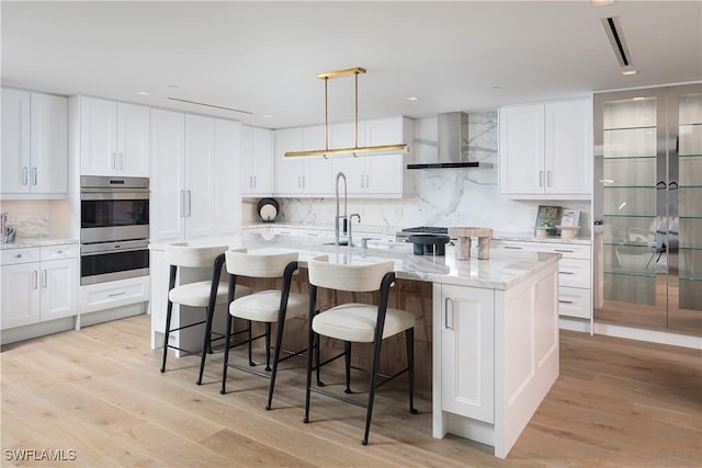 6897 Grenadier Blvd Unit 1602, Naples, FL 34108 - kitchen with white cabinets, light wood-style floors, wall chimney exhaust hood, and backsplash