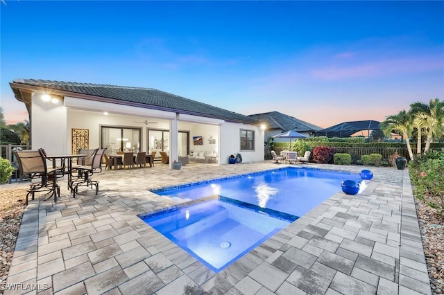 pool at dusk featuring a patio area, a ceiling fan, outdoor dining area, fence, and an in ground hot tub