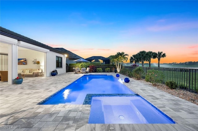 pool at dusk with a fenced backyard, a patio, a pool with connected hot tub, and an outdoor hangout area