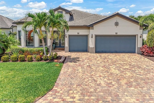 view of front of property featuring stucco siding, a tile roof, decorative driveway, a front yard, and a garage