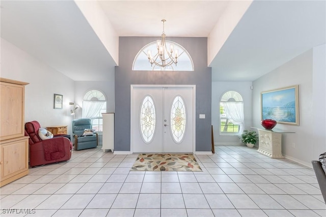 foyer entrance featuring an inviting chandelier, light tile patterned floors, high vaulted ceiling, and baseboards